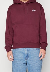 Sudadera color burdeos hecha de una suave mezcla de algodón, con un bolsillo delantero, puños acanalados y un logotipo blanco de Nike en el pecho.