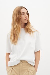 Hvid kortærmet t-shirt i et blødt materiale, med rund halsudskæring og en afslappet pasform, parret med lyse khaki bukser.