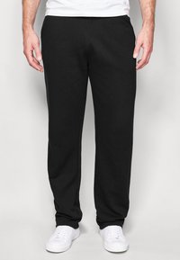 Pantalones deportivos negros de tejido de mezcla de algodón, con un diseño de pierna recta y cintura elástica, combinados con zapatillas blancas.