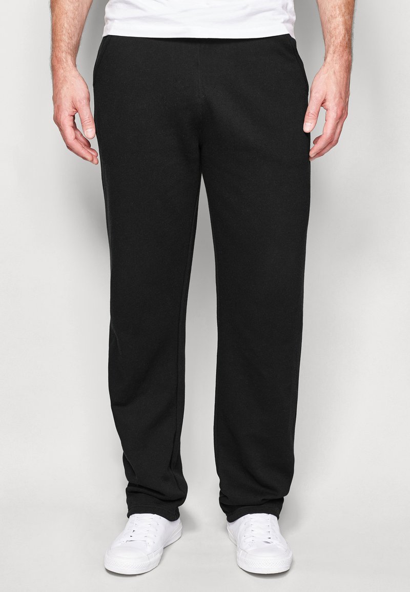 Pantalones deportivos negros de tejido de mezcla de algodón, con un diseño de pierna recta y cintura elástica, combinados con zapatillas blancas.