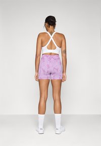 Soutien-gorge de sport blanc avec un dos croisé, assorti à un short rose tie-dye. Les deux vêtements sont confectionnés dans un matériau ajusté et extensible.