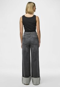 Svart ärmlös topp i kombination med vida mörkgrå jeans med fransade fållar och kontrasterande ljusgrå tyg vid muddarna.