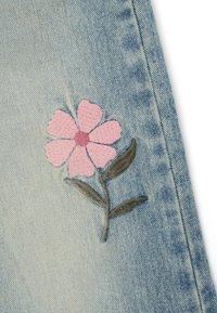 Tejido de mezclilla de color azul claro con una flor bordada en rosa de cinco pétalos y hojas verdes, que muestra una textura suave y costuras detalladas.