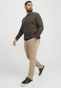 Hnědá mikina, béžové kalhoty, černé tenisky. Modelka kráčí s rukama v kapsách, ukazujíc, jak dobře padne a jaký má uvolněný styl.