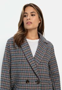 Dubbelzijdige jas gemaakt van gestructureerd materiaal met een multicolore houndstoothpatroon. Bevat grote bruine knopen en een gekraagde hals.