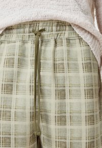 Plaid loungedragter i creme og olivengrøn, med snøre i taljen og blødt, tekstureret stof med et ternet mønster.