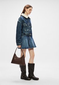 Τζάκετ τζιν με γούνα στο γιακά, σε συνδυασμό με τζιν φούστα, καφέ δερμάτινες μπότες μέχρι το γόνατο και καφέ τσάντα hobo.