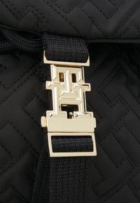 Fermeture à boucle géométrique dorée sur une sangle tissée noire, sur un tissu noir matelassé avec des motifs en losanges cousus.