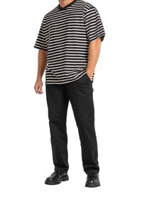 Pruhované tričko s krátkými rukávy v černé a krémové barvě, kombinované s černými kalhotami a černými botami. Ležérní střih a jednolitý materiál.