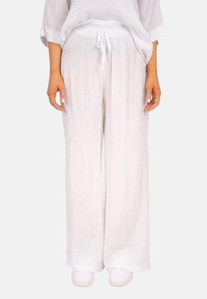 Pantalon large blanc en tissu léger et texturé, avec une taille élastique et un cordon de serrage. Porté avec des chaussures blanches.