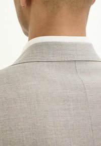 Giacca da suit grigia chiara con una texture liscia, caratterizzata da un rever strutturato e cuciture pulite lungo la cucitura posteriore.