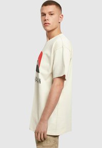 Camiseta color crema hecha de algodón suave, con un diseño gráfico que presenta un corazón rojo, montañas y la palabra "JAPÓN" en negro.
