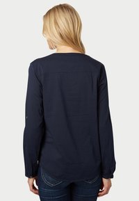 Chemise à manches longues bleu marine avec un motif texturé, encolure arrondie et poignets boutonnés. Présente un empiècement au dos.