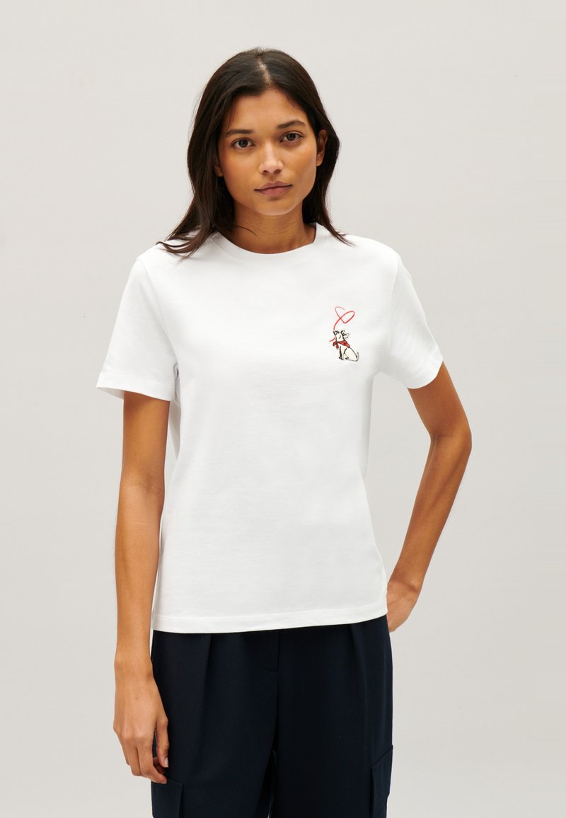 T-shirt en coton blanc avec un col rond, des manches courtes et un petit motif rouge brodé représentant un personnage tenant un cœur.