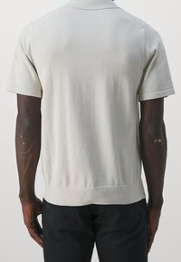 Poloko s krátkým rukávem ve světlé šedé pletenině. Má žebrovaný límeček a lem, s hladkou texturou a přiléhavým střihem.