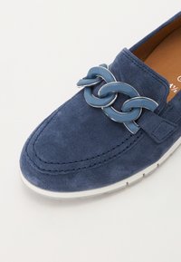 Kék velúr slip-on cipő, amely kiemelkedő kék lánccal és fehér gumitalppal rendelkezik; kerek orr, varrott részletezéssel.
