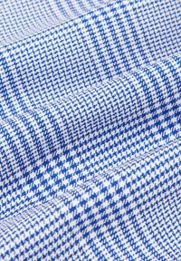 Woven fabric featuring a blue and white houndstooth pattern with a textured surface, displaying a diagonal arrangement of small shapes.