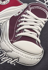 Grafiska ilustrācija ar ķiršu sarkanām sneakerām ar baltām auklām, gumijas pirkstu daļu un detalizētu izšūšanu uz tumša fona.