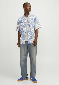 Korte mouwen shirt met een blauw en beige geometrisch patroon, gecombineerd met losse grijze denim jeans en blauwe sneakers met witte accenten.