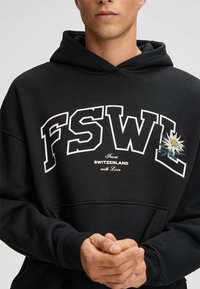 Felpa nera con cappuccio caratterizzata dalle lettere "FSWL" in bianco, con il testo "From SWITZERLAND with Love" e un motivo floreale ricamato. Tessuto morbido.
