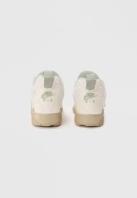 Białe i jasnoszare sneakersy Nike Air z teksturowaną beżową podeszwą, z wyściełanym kołnierzem, logo oraz charakterystycznym wzorem pięty.