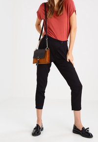 Pantaloni neri a vita alta, maglietta rossa e mocassini neri, con una borsa a tracolla marrone e nera dotata di una patta testurizzata e di una tracolla a catena.