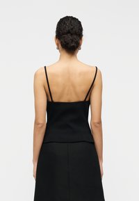 Μαύρο καμισόλι με λεπτούς ιμάντες σπάγγου, εφαρμοστή σχεδίαση, λεία υφή και ελαφρώς καμπανοειδές τελείωμα. Βλέπεται από πίσω.
