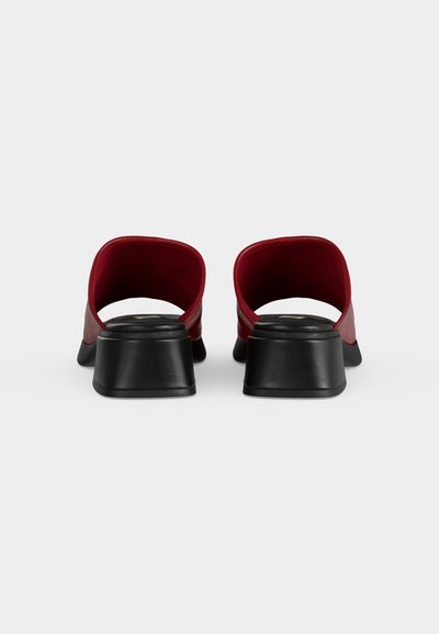 Ζευγάρι κόκκινα παπούτσια mule με μαύρα τετράγωνα τακούνια, σε θέα από πίσω σε λευκό φόντο.