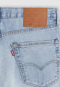 Poche arrière d'un jean Levi's bleu clair avec surpiqûres orange, étiquette rouge Levi's et patch en cuir marron indiquant la marque et le modèle 501.