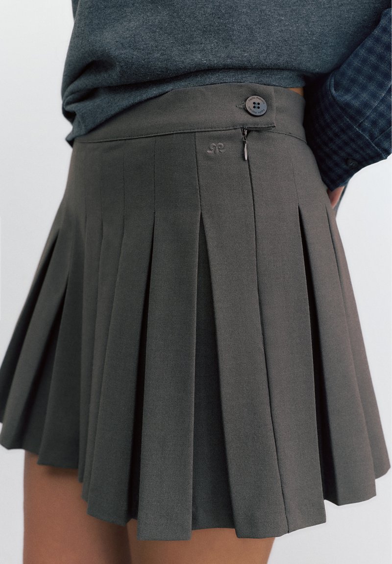 Ciemnoszara plisowana spódnica z bocznym suwakiem i guzikiem, noszona z wpuszczonym do środka ciemnoszarym topem.