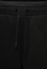 Κοντινό πλάνο στη μέση μαύρου φλις παντελονιού με κορδόνια δεσίματος, παρουσιάζοντας υφή υφάσματος και λεπτομέρειες ραφών.