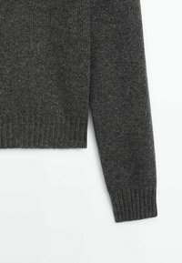 Manche et ourlet inférieur d’un pull en tricot gris foncé avec poignets et ceinture côtelés, présentés sur fond blanc.