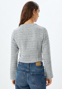 Grå texturerad kort tröja med rutmönster och långa ärmar, tillsammans med blå jeans med hög midja som har bakfickor.