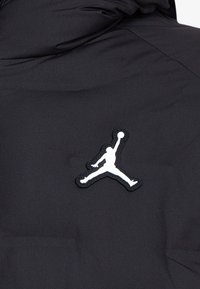 Giacca imbottita nera con logo Jumpman ricamato bianco sul petto. Il materiale ha una texture liscia e opaca.