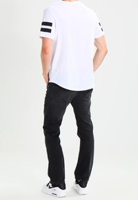 Camiseta blanca con acentos de rayas negras en las mangas, combinada con jeans negros y zapatillas blancas. Ajuste casual con un diseño de pierna recta.