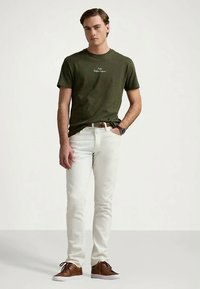 Λαδί βαμβακερό t-shirt με στρογγυλή λαιμόκοψη; λευκό τζιν παντελόνι; καφέ δερμάτινα αθλητικά παπούτσια; μινιμαλιστικός σχεδιασμός, χωρίς ορατά σχέδια ή λογότυπα.