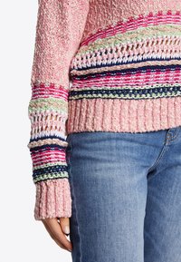 Strickpullover mit einem Muster aus pinken und mehrfarbigen Streifen, gerippten Säumen und offenen Akzenten an den Ärmeln, kombiniert mit blauen Jeans.