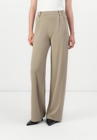 Beige wide-leg trousers made from a smooth fabric, featuring gold-tone hardware accents and structured waistband. Paired with pointed black heels.