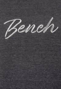 Dunkelgrauer Baumwollstoff mit weiß gesticktem Text "Bench" in kursiver Schriftart, mit einer glatten Textur und subtilen Schattierungsvariationen.