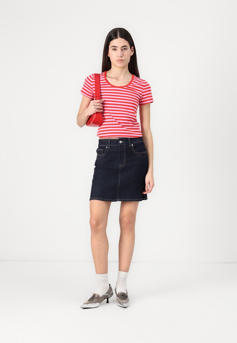 T-shirt à rayures rouges et blanches à manches courtes associé à une mini-jupe en denim foncé, des chaussures argentées à bout pointu et un petit sac à main rouge.