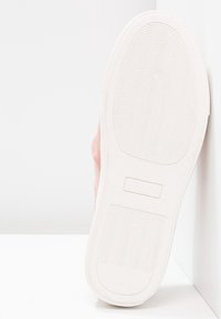 Semelle d'une chaussure rose avec un motif de semelle ondulé, taille 37, positionnée verticalement contre des murs et un sol blancs.