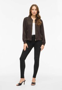 Brūna zamšādas bombermodela jaka ar rāvējslēdzēja priekšpusi, ribotu aproču un apakšmala. Kombinēta ar melnām pieguļošām džinsiem un melnām papēžainām mulām.