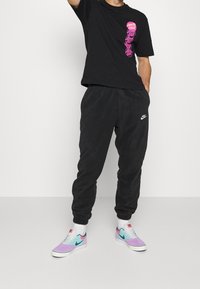 Svart t-shirt med rosa grafik, svarta sweatpants och flerfärgade sneakers med lila och blå detaljer. Avslappnad outfit med synlig logotyp.