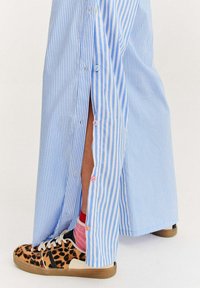 Pruhovaná modro-bílá sukně s bočními knoflíky a vysokým rozparkem, spárovaná s teniskami s leopardím potiskem a vrstvenými barevnými ponožkami.