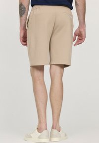 Shorts beiges avec une taille élastique, des poches latérales et une poche arrière unique, fabriqués à partir d'un tissu lisse. Portés avec des baskets claires.