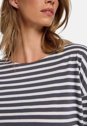 Frau trägt ein schwarz-weiß gestreiftes Shirt mit rundem Ausschnitt, zeigt einen Teil ihres Gesichts und schulterlanges Haar.