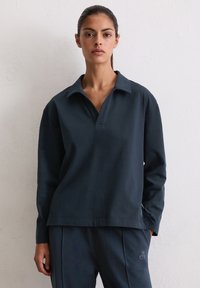 Granatowy pulower wykonany z miękkiego materiału, z szerokim kołnierzem i luźnym krojem. Wyraźny detal z logo po boku oraz eleganckie przeszycia.