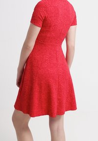 Kortärmad röd klänning med ett blommigt texturmönster, utsvängd kjol och figursydd bodice, med rund halsringning och bakre sömdetalj.