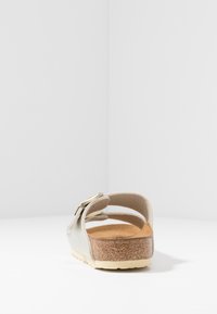 Sölvfärgad lädersandal med en korkfotbädd, justerbar spännestraps, och strukturerad yttersula; minimalistisk design med en platt profil.