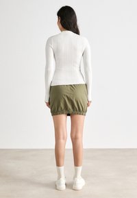 Hvit stripete langermet topp kombinert med grønn mini-skjørt med snor, som har samlet kant, båret med hvite joggesko og kremfargede sokker.